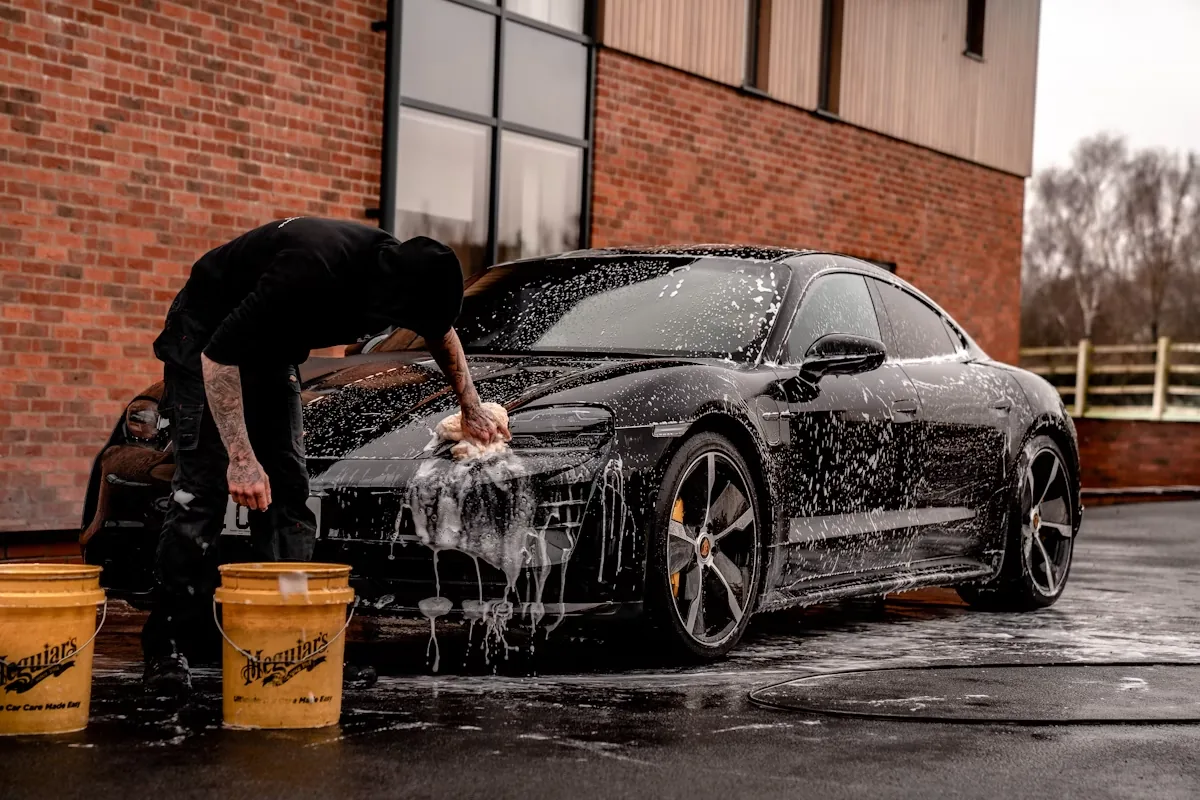 A detailer covering a black saloon in thick snow foam during an exterior wash
