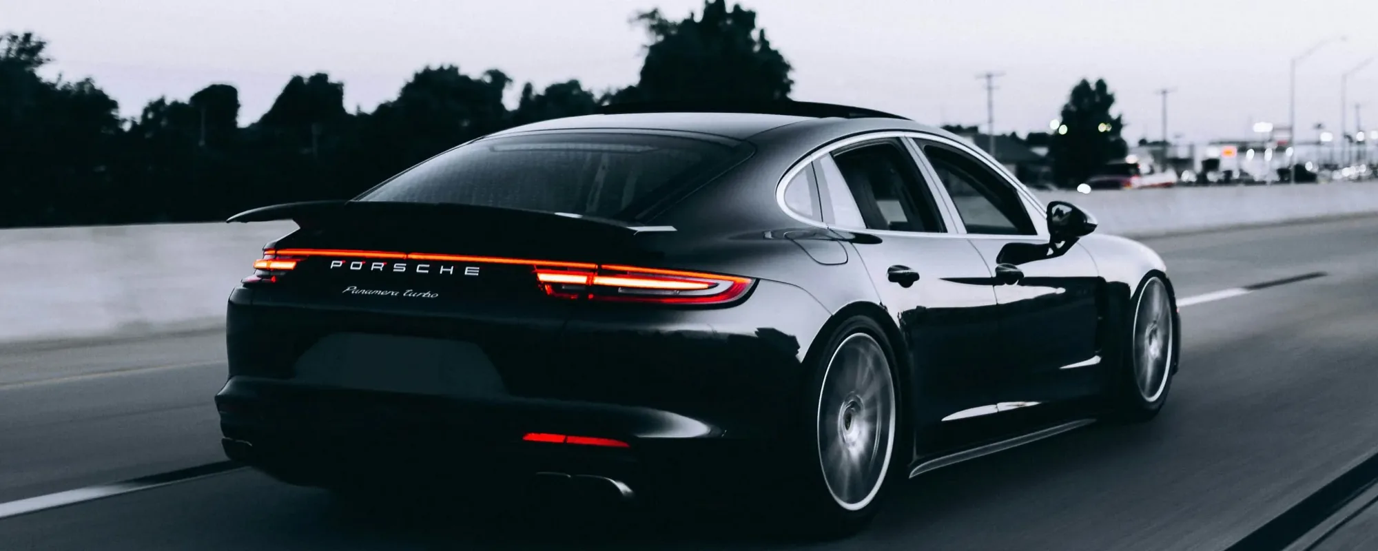 A black Porsche Panamera with a mirror-gloss finish on the highway at dusk