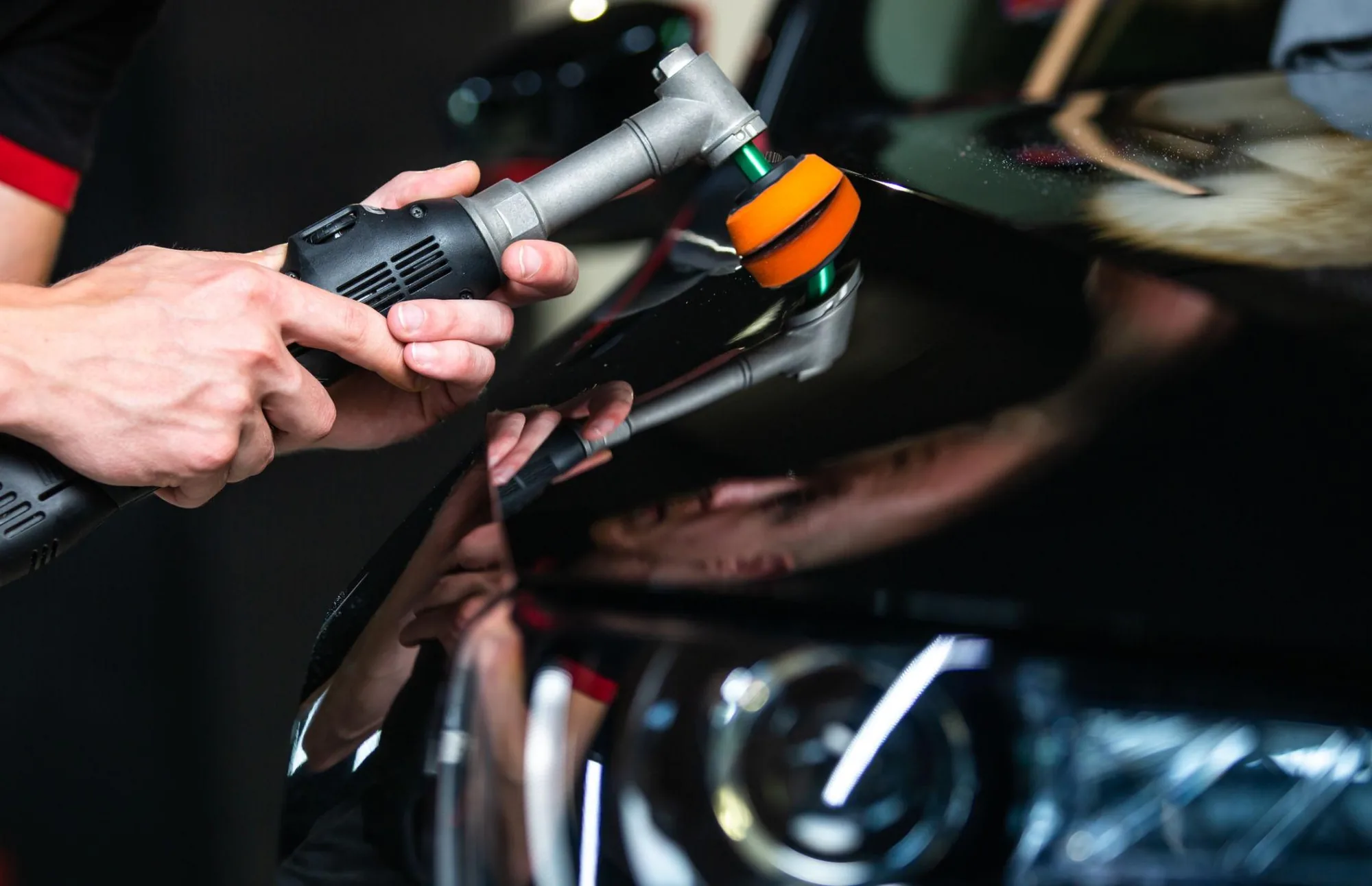 A detailer running a dual-action polisher across a headlight and front wing